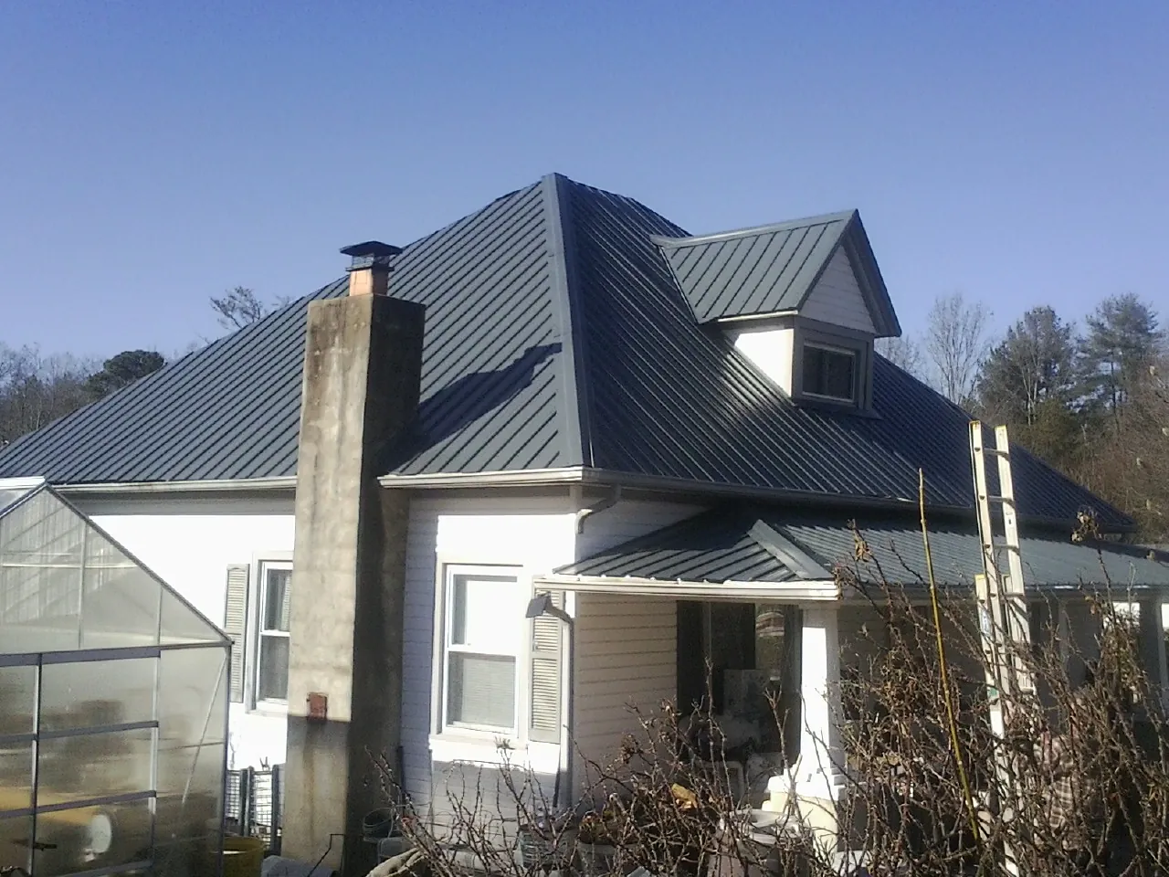Dark blue standing seam metal roof on a white farmhouse with dormer — Slate & Tile Roof Repair by Roofing Brothers in Akron