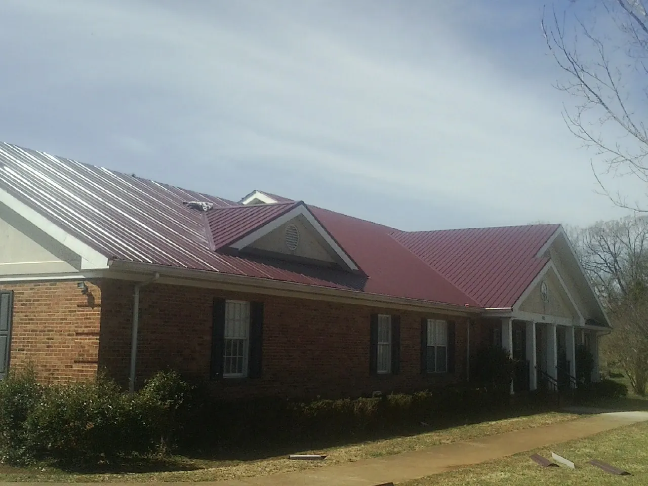Red metal roof with gabled entries on a long brick building, from a Hail Damage Roof Repair job in Akron